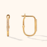 Gold-tone rectangular hoop earrings with rounded corners and rows of clear accents, shown from front and side on a cream background.