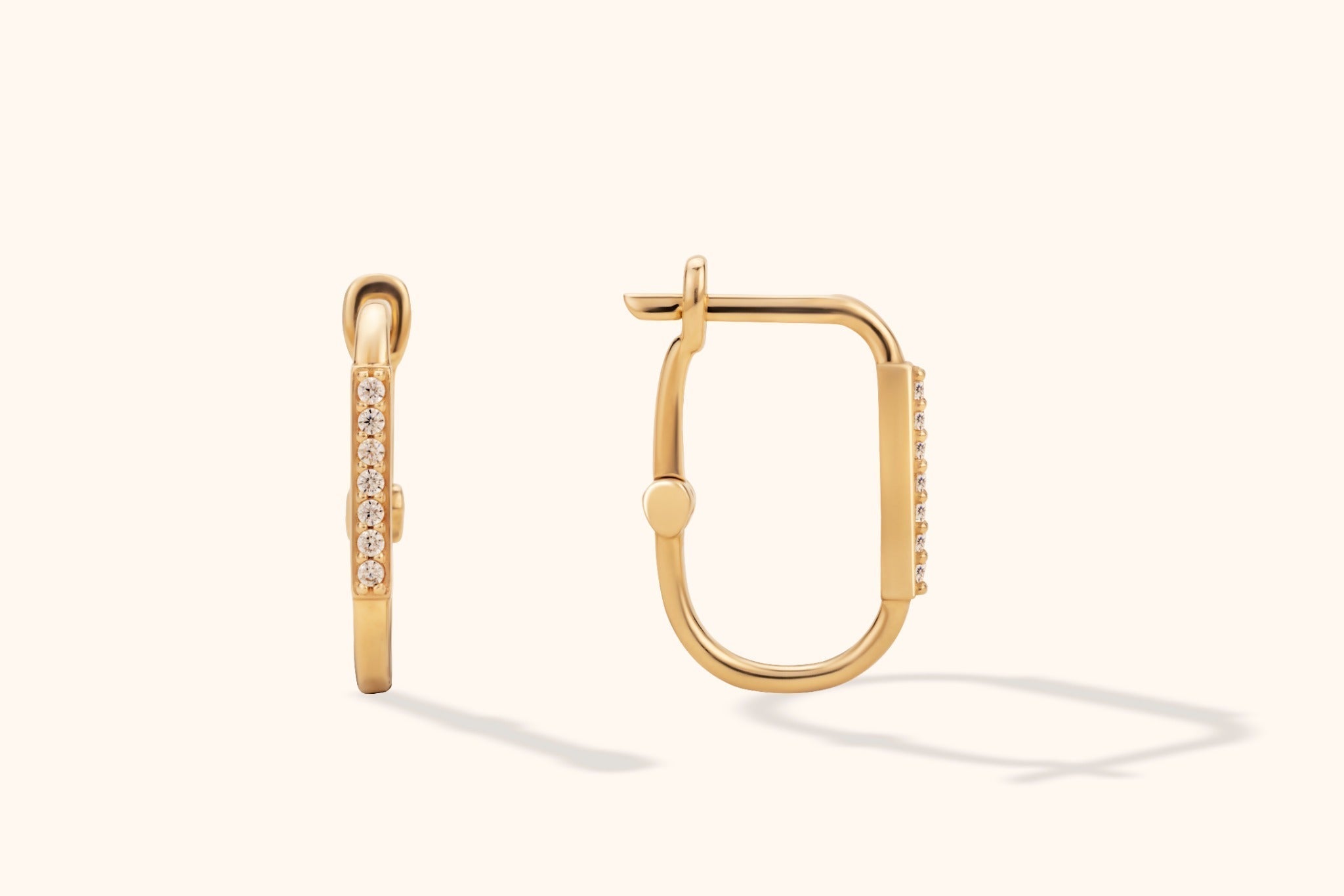Gold-tone rectangular hoop earrings with rounded corners and rows of clear accents, shown from front and side on a cream background.