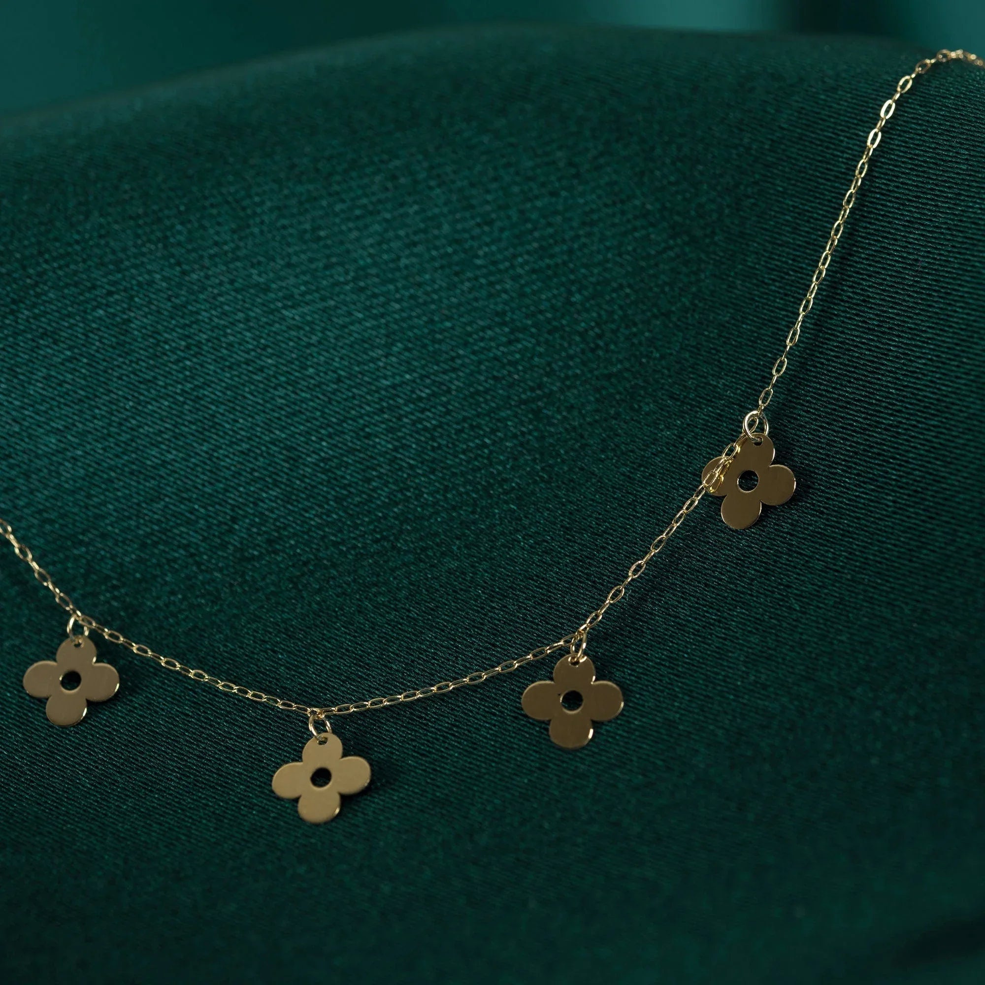 14K gold necklace featuring multiple four-leaf clover charms, styled on deep green satin background.