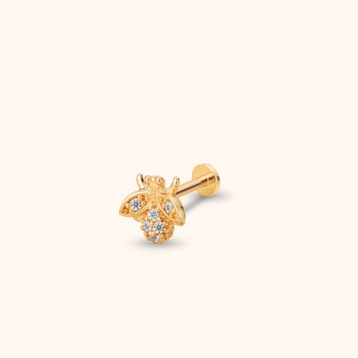 Gold-colored bee stud earring with clear sparkling accents, a straight post and flat round back on a pale cream background.