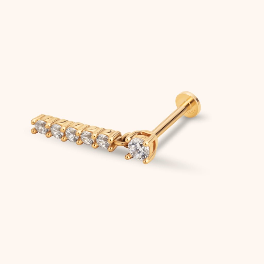 Gold-colored flat-back earring with a round clear stone and a dangling straight bar set with five smaller clear stones.