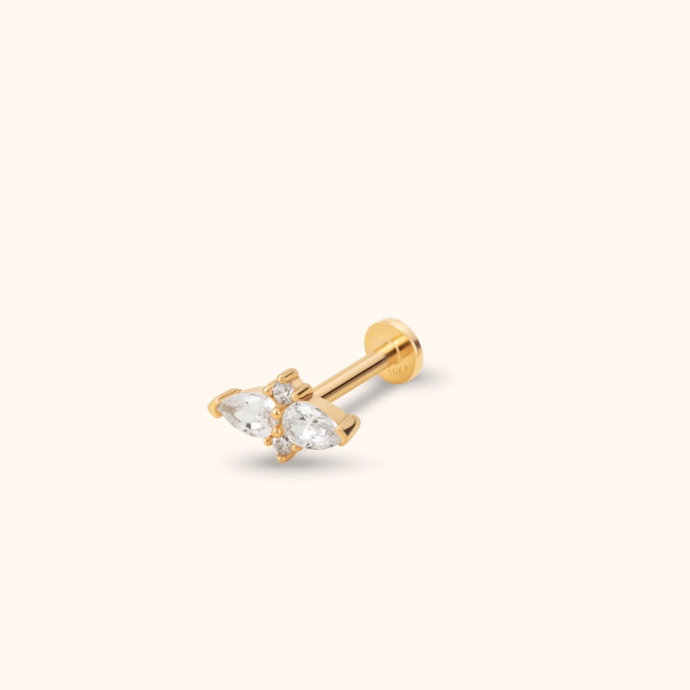Gold-tone flat-back stud with two clear teardrop-shaped stones and small round accents, shown at an angle on a cream background.