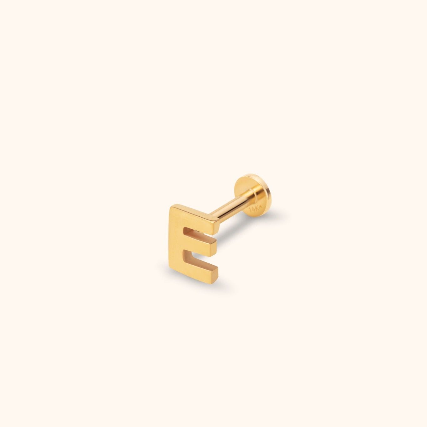 Gold-toned letter E stud earring with a straight post and round flat back, shown at an angle on a cream background.