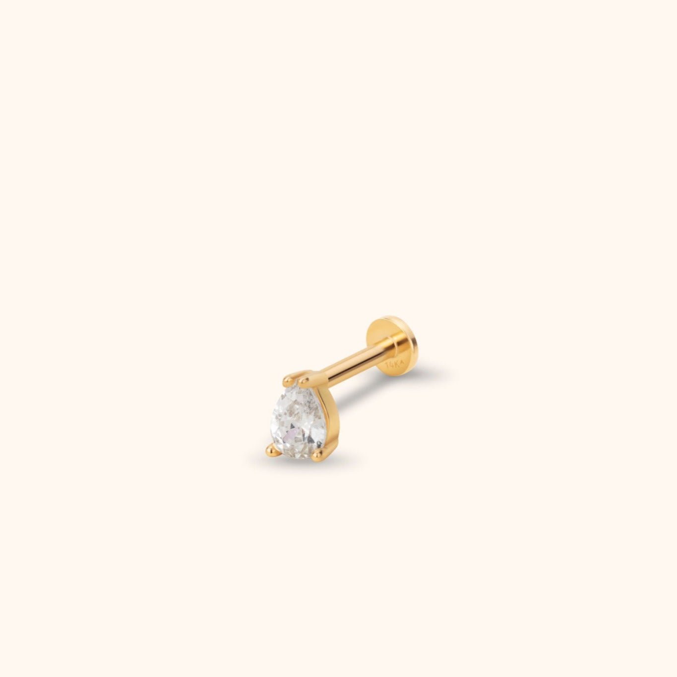 Gold-toned stud with a clear teardrop-shaped faceted center, prong setting and round flat back on a cream background.