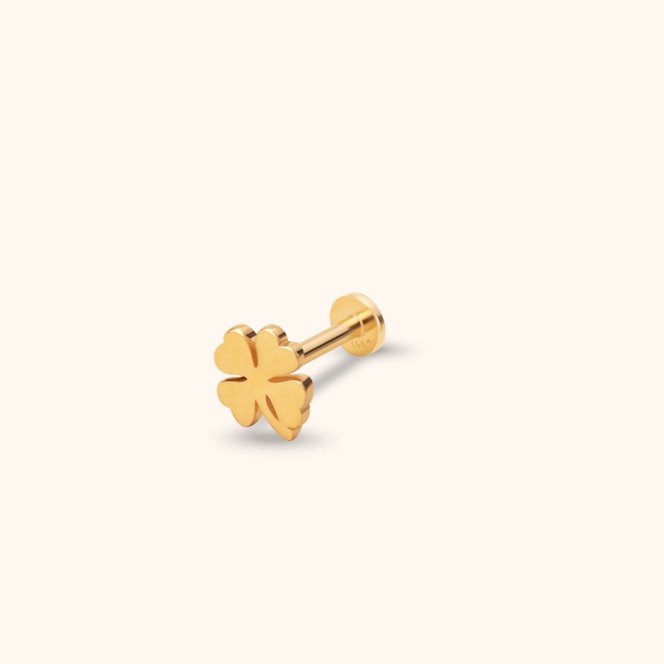 Gold-colored four-leaf clover stud with a straight post and flat circular back, shown at an angle on a cream background.