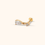 Gold-toned flat-back stud with a small round clear stone and a dangling pear-shaped clear stone on a cream background.
