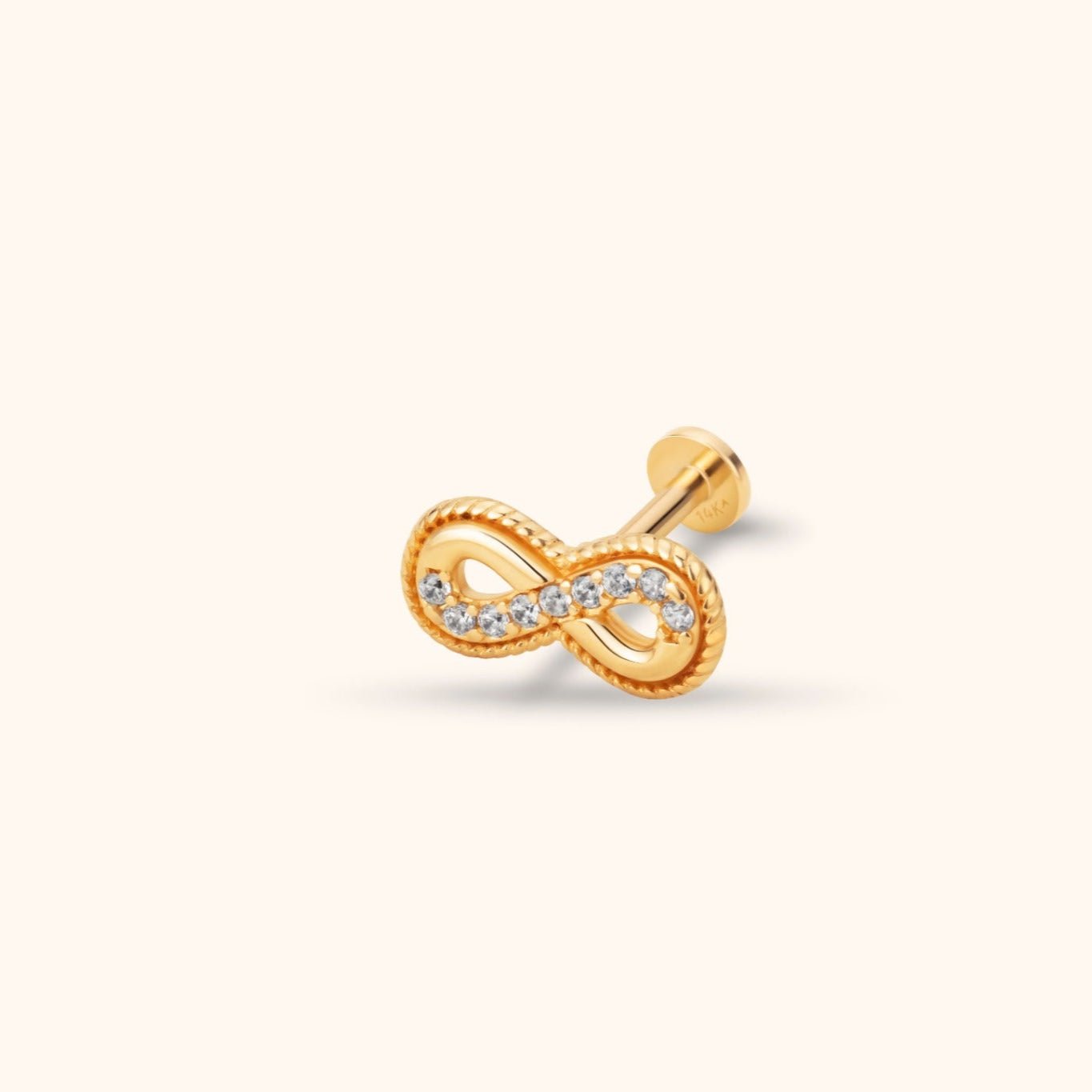 Gold-colored infinity stud with a ridged border, a row of clear stones and a round flat back, shown on a cream background.