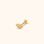 Gold-colored eye-shaped stud with radiating lashes, a clear faceted center, straight post and round flat back on a cream background.