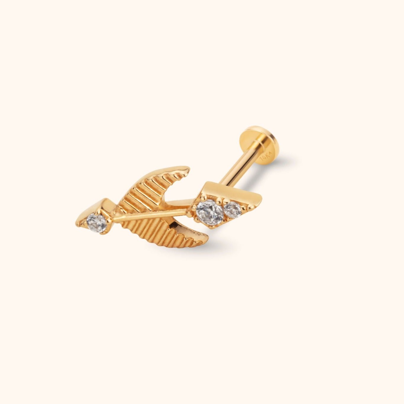 Gold-colored arrow stud with ridged feather details, three clear round accents, and a flat circular back on a cream background.