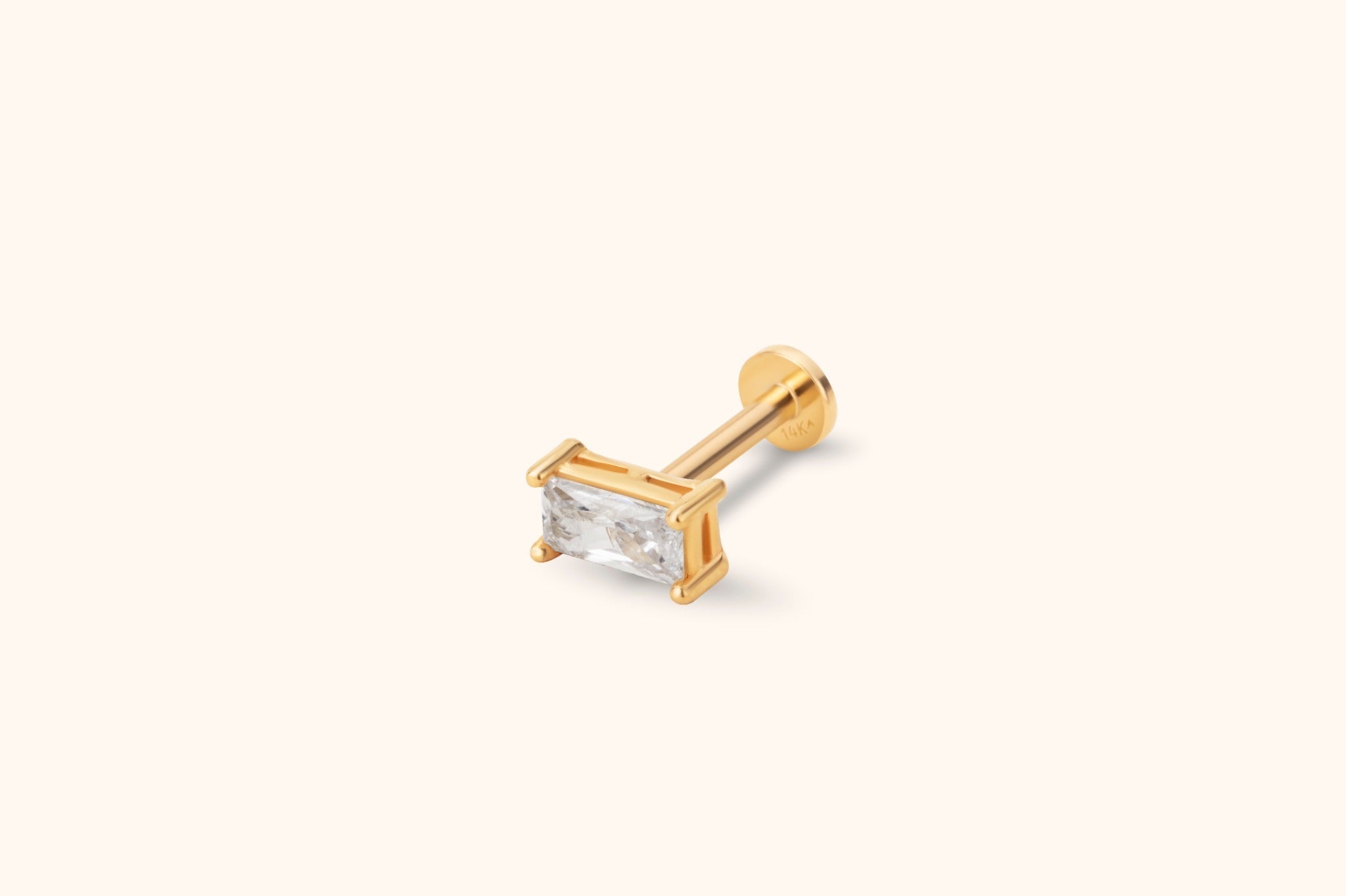 Gold-toned stud earring with a clear rectangular faceted stone, straight post and round flat back on a cream background.