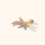 Gold-toned shooting star stud with small clear accents, a straight post and round flat back on a cream background.