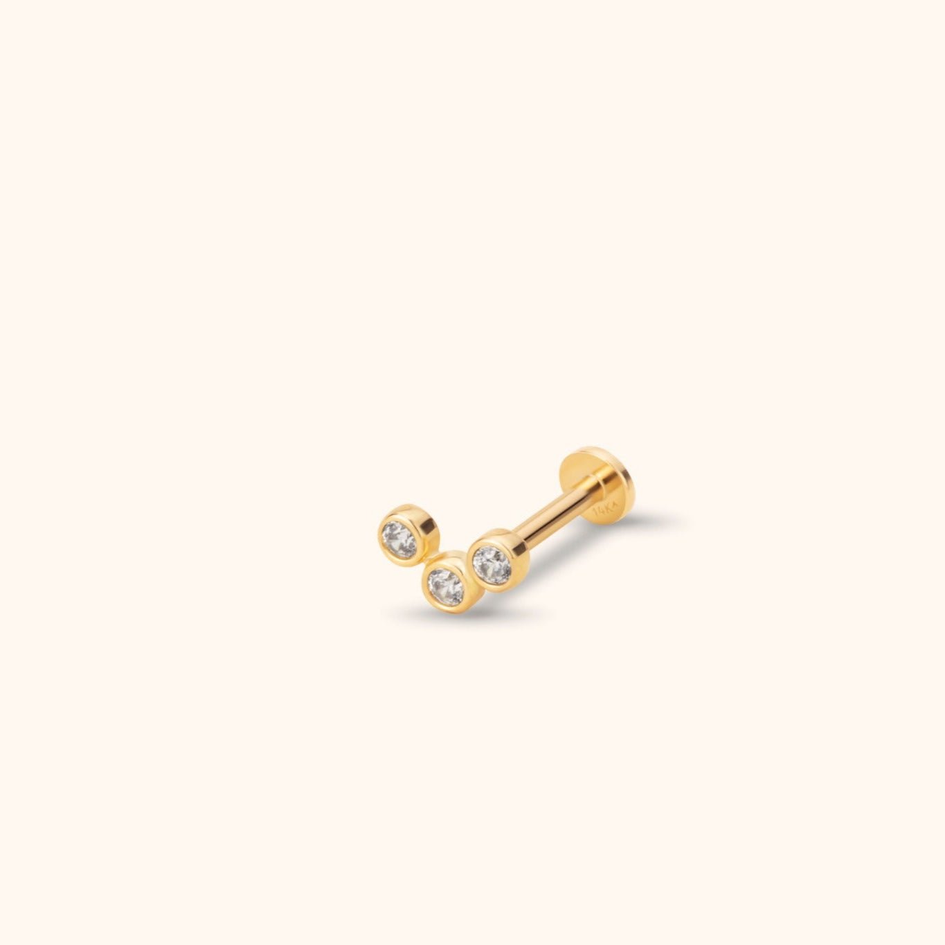 Gold-toned piercing stud with three clear round accents in a V-shaped bezel cluster, a straight post and flat disc back.