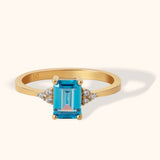 14K gold ring with emerald-cut blue topaz and side diamond clusters