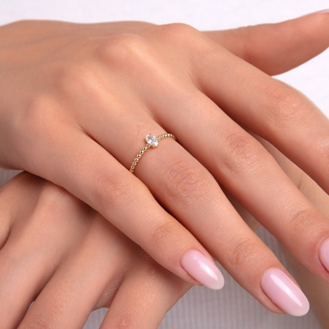 Close-up of a delicate gold ring with beaded texture and a single round stone on a woman's hand