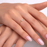 Close-up of a delicate gold ring with beaded texture and a single round stone on a woman's hand