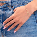 Woman wearing a 14K gold plated minimalist bracelet with three blue bezel-set crystals, styled with denim jeans