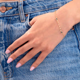 Woman wearing a 14K gold plated minimalist bracelet with three blue bezel-set crystals, styled with denim jeans