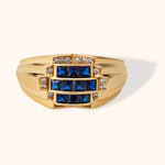 14K gold statement ring with blue baguette sapphires and cubic zirconia on cream background.