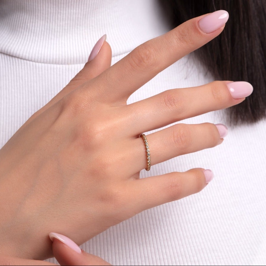 Elegant woman wearing a classic gold eternity ring with cubic zirconia stones, styled with a white turtleneck and soft pink nails.

