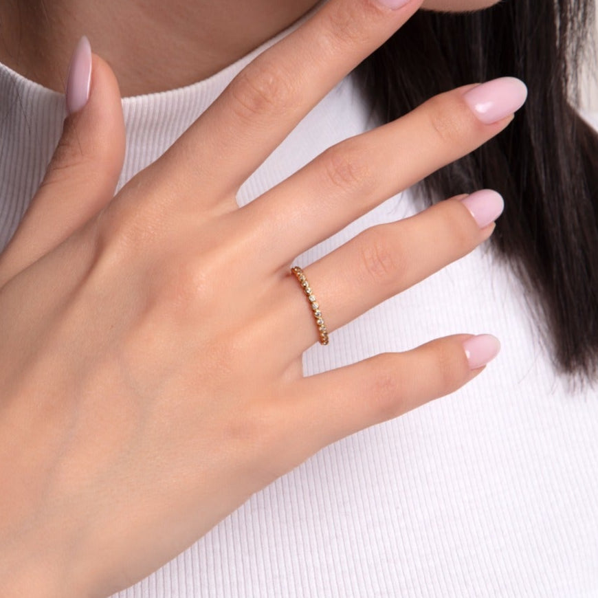 Elegant full eternity ring with round-cut stones set in gold, worn by a woman with soft pink manicure and minimal gold bracelets.

