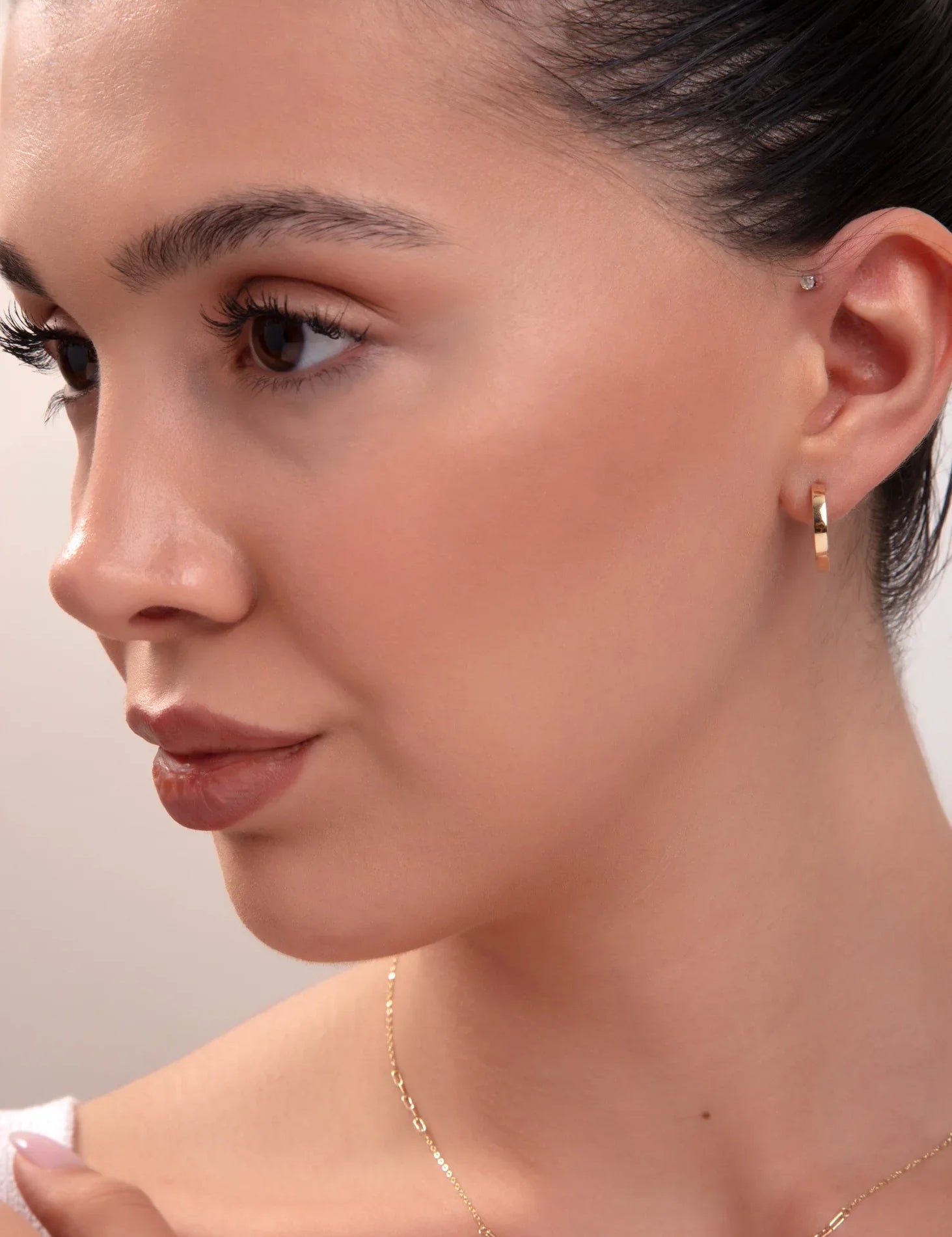 Close-up of model wearing classic small gold hoop earring and minimal gold necklace

