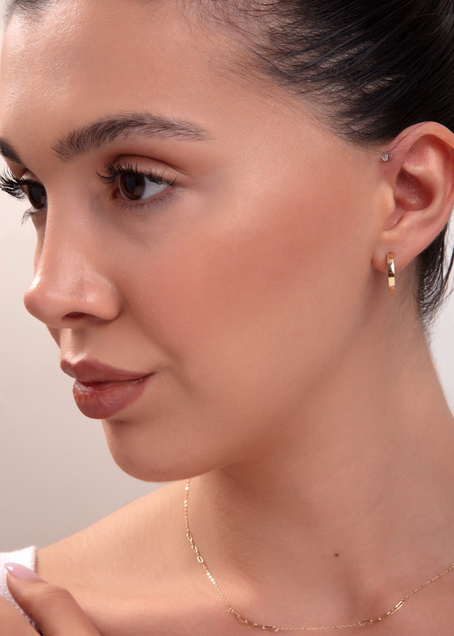 Close-up of model wearing classic small gold hoop earring and minimal gold necklace

