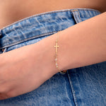 Minimal gold bracelet with cross charm and crystal beads on wrist, styled with denim

