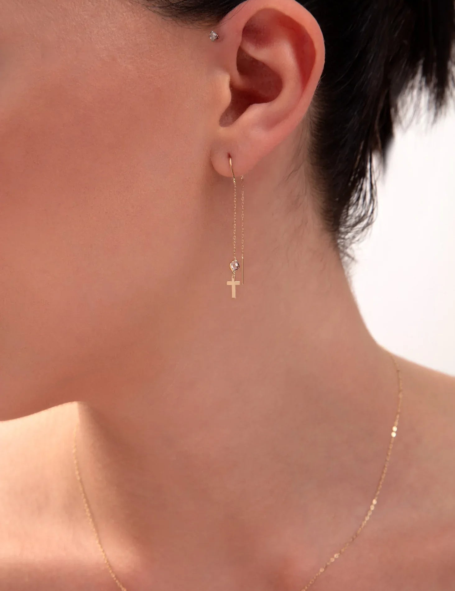 Gold threader earring with cross charm and crystal bead on model's ear

