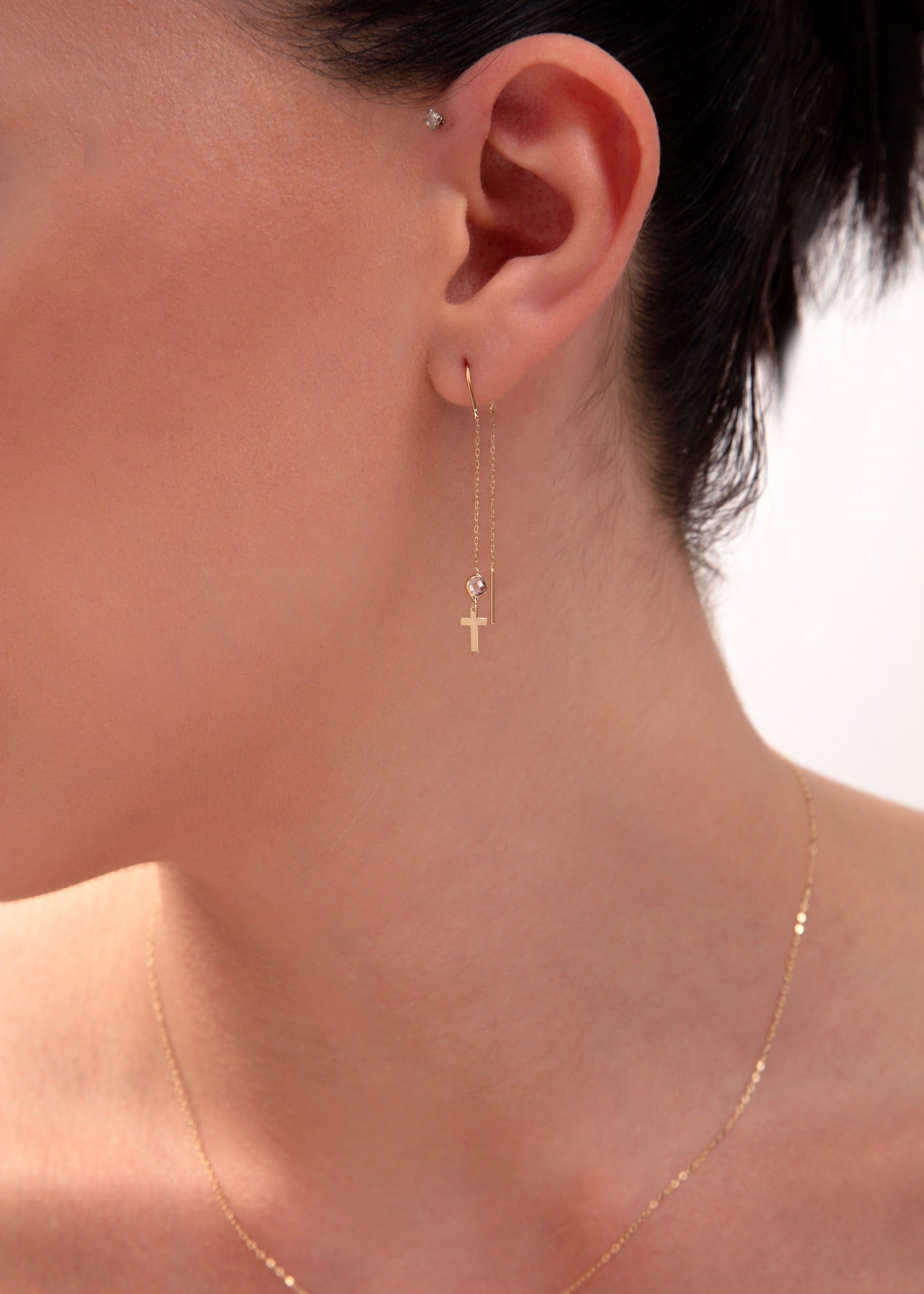 Gold threader earring with cross charm and crystal bead on model's ear

