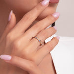Close-up of a woman’s hand and lips, showcasing a 14K gold evil eye band ring with alternating blue enamel charms and white stones in a delicate pattern.