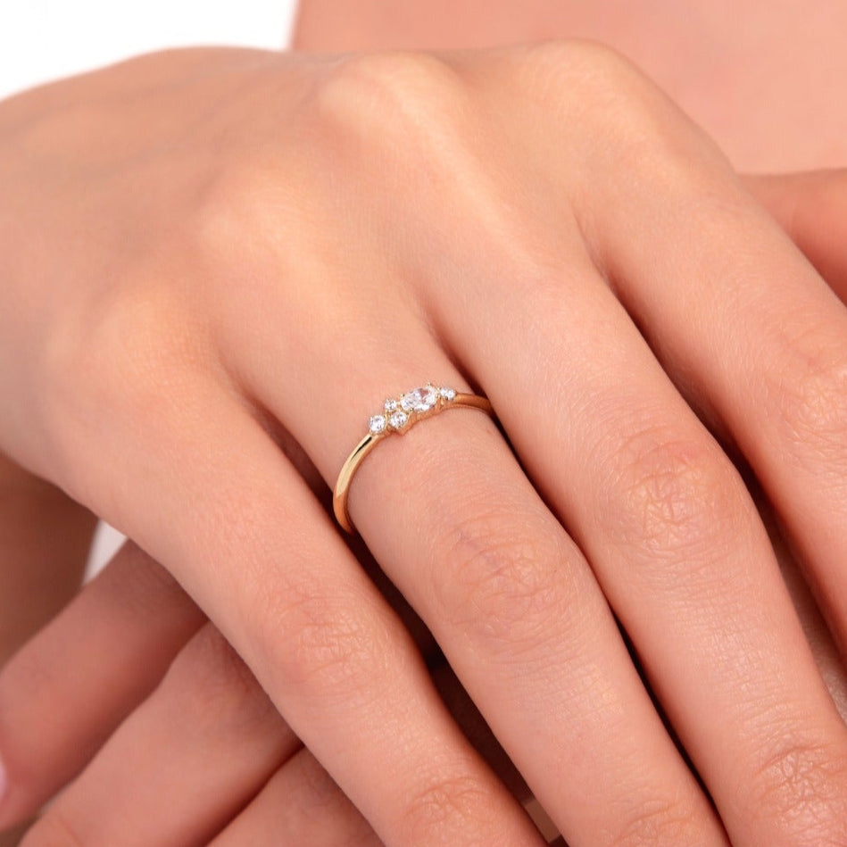 Close-up of a woman's hands wearing a dainty 14K gold ring with three sparkling zirconia stones.
