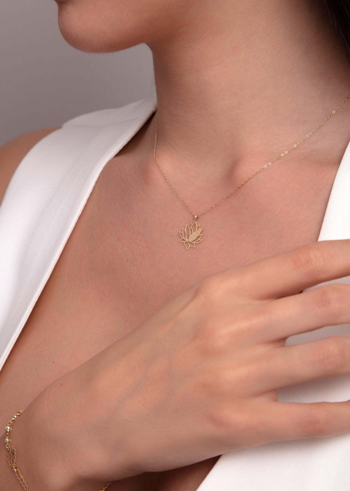 Close-up of a woman's neck wearing a delicate 14K gold lotus flower pendant necklace on a fine chain.