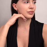 Close-up of a woman wearing a 14K gold lotus necklace and minimalist gold earrings, styled with a deep V-neck black top — showcasing a calm and elegant expression.