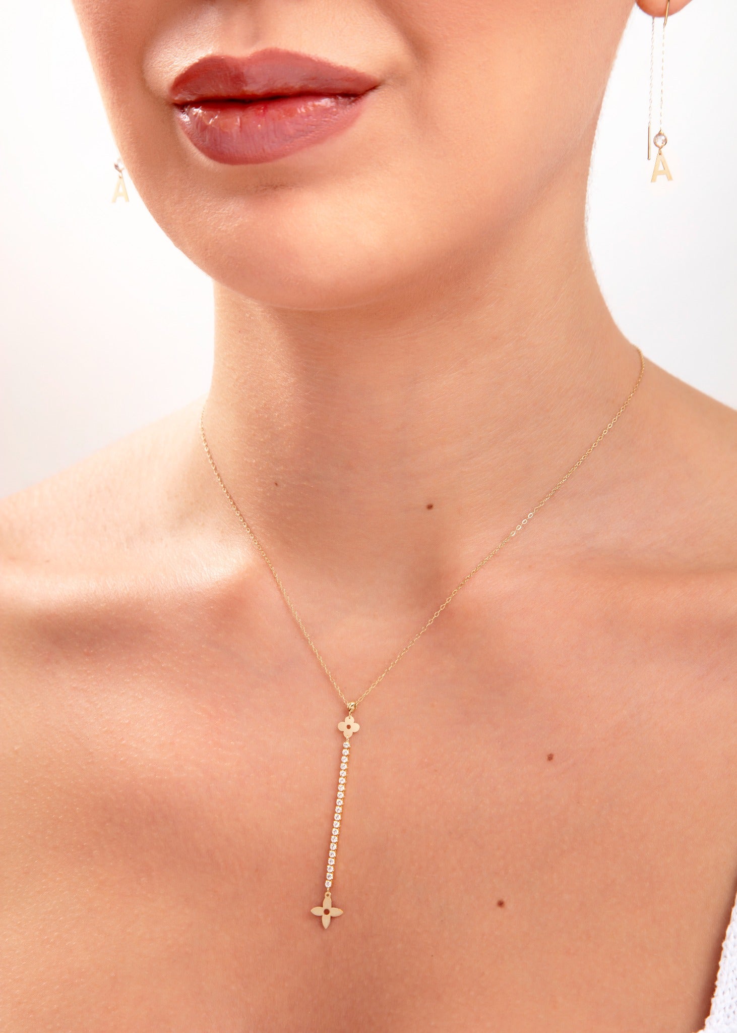 Close-up of woman wearing a 14K gold plated floral pendant necklace with vertical crystal bar and initial letter "A" earrings

