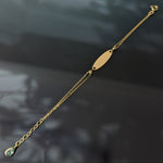 14K gold baby ID bracelet for boys with a blue gemstone accent and engravable nameplate, displayed on a black reflective background