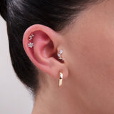 Curated ear stack featuring a trio of 14K gold cartilage studs: a floral CZ cluster in the helix, a larger flower stud in the middle cartilage, and a marquise leaf-shaped CZ earring in the inner conch – Finished with a polished gold hoop in the lobe