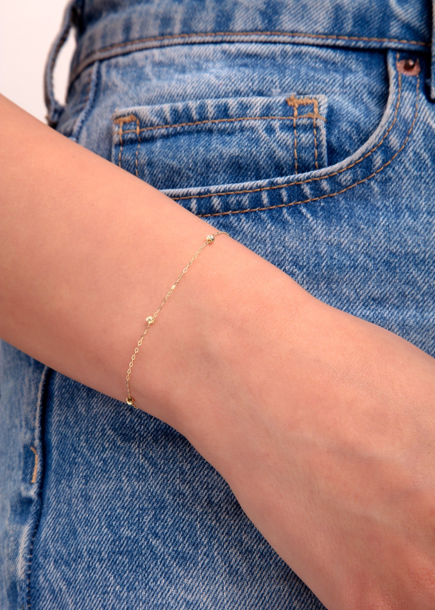 Minimalist gold bead bracelet on wrist with denim background, dainty jewelry close-up

