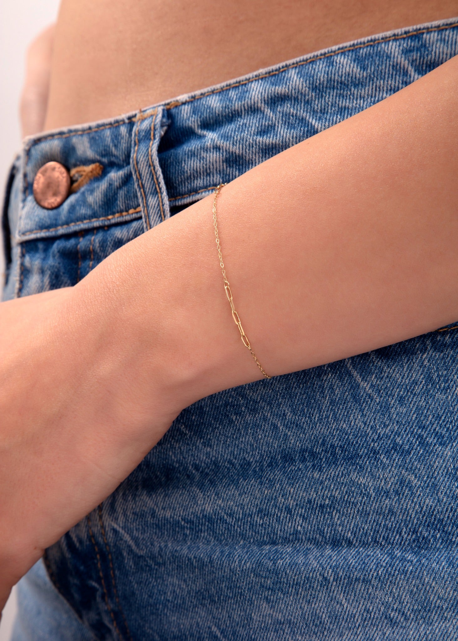 Close-up of a dainty gold chain bracelet on wrist, styled with blue denim jeans

