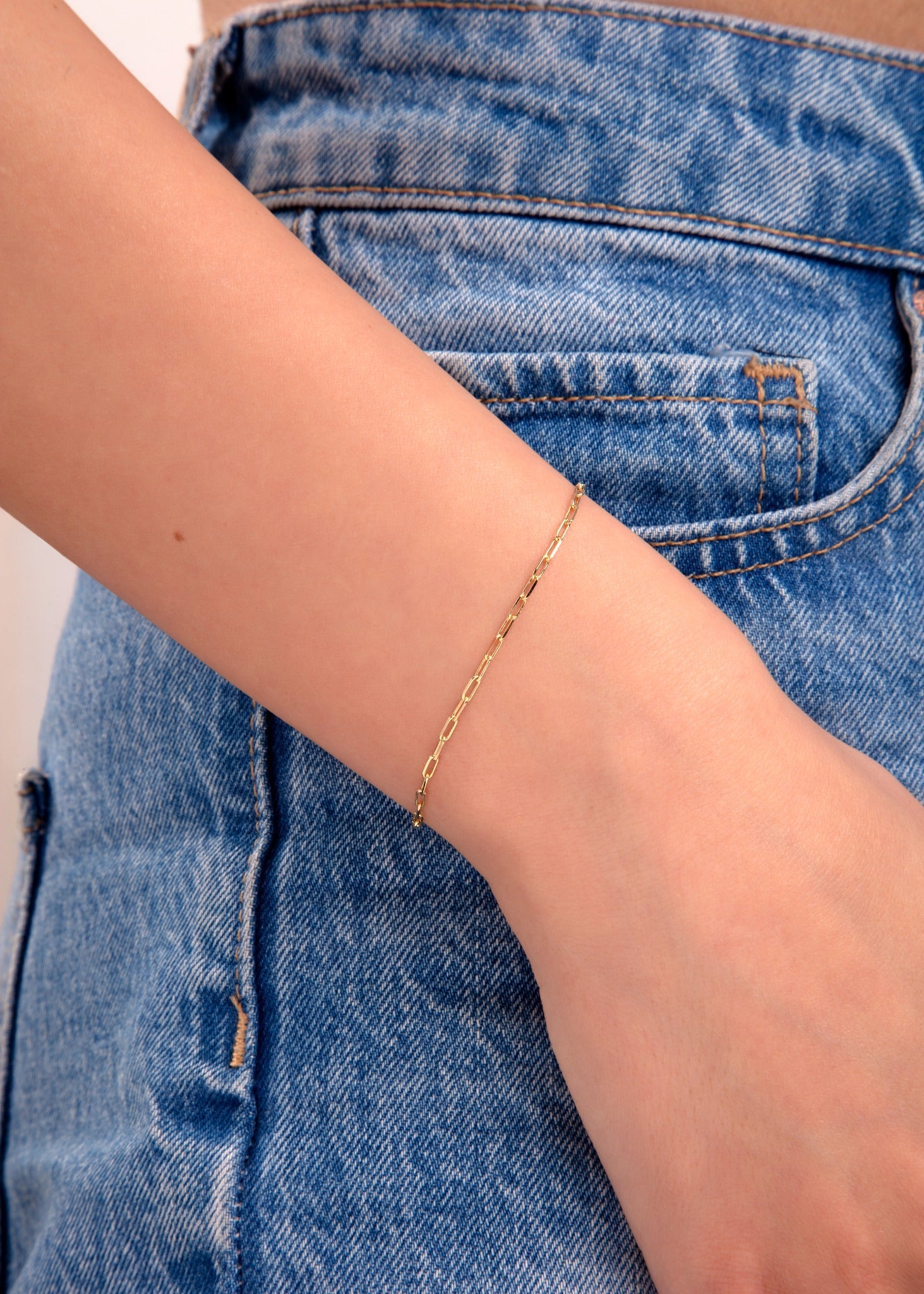 Minimalist gold paperclip chain bracelet on wrist with denim jeans background

