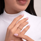 Delicate gold ring adorned with evenly spaced round-cut diamonds, worn on a woman's hand with pale pink nails, styled with a white turtleneck for an elegant, minimalist look.

