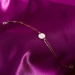 14K gold bracelet with a personalized round disc charm on a double chain, presented on a purple satin background