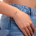 Close-up of woman wearing a 14K gold plated bracelet with dotted emerald green crystals, styled with denim jeans

