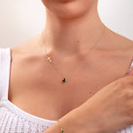 Woman wearing a 3-piece emerald green jewelry set including side cross necklace with teardrop, matching threader earrings, and dotted green stone bracelet

