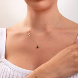 Woman wearing a 3-piece emerald green jewelry set including side cross necklace with teardrop, matching threader earrings, and dotted green stone bracelet

