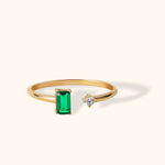 14K gold open ring featuring a green emerald baguette and a round white diamond
