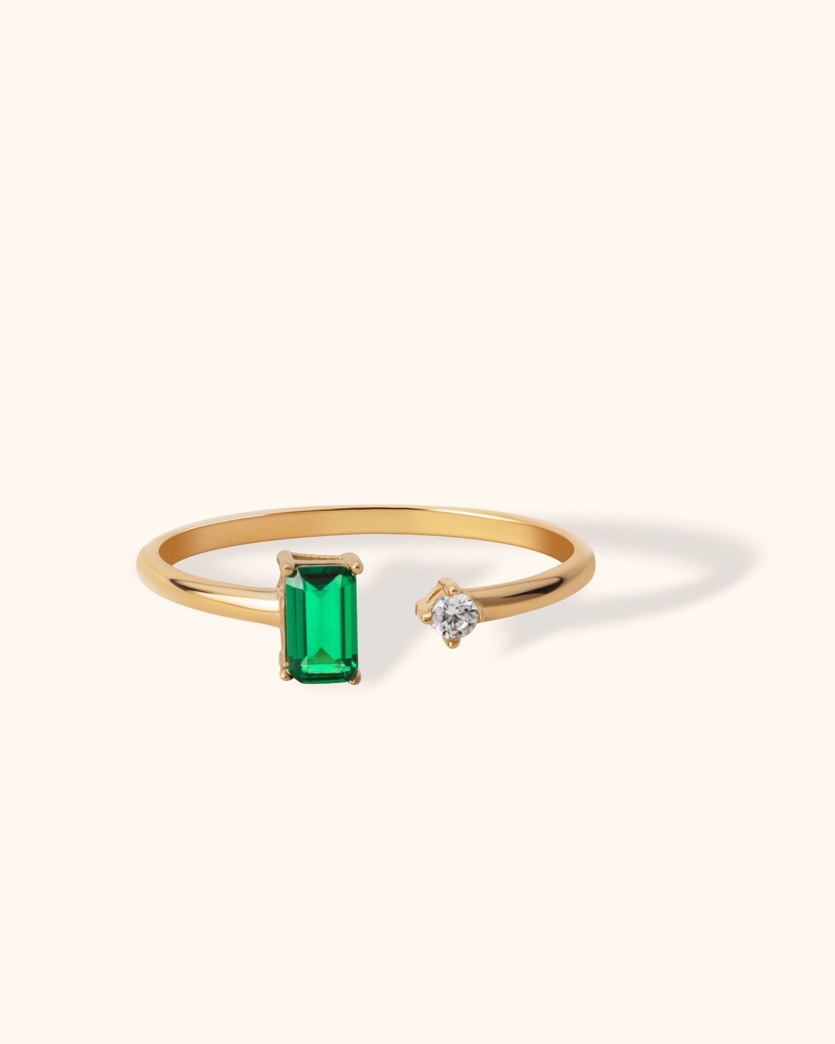 14K gold open ring featuring a green emerald baguette and a round white diamond