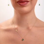 Model wearing a 14K gold plated necklace with emerald teardrop crystal and horizontal gold cross, paired with matching green teardrop threader earrings

