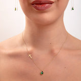 Model wearing a 14K gold plated necklace with emerald teardrop crystal and horizontal gold cross, paired with matching green teardrop threader earrings

