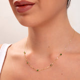 Model wearing gold necklace with green gemstones

