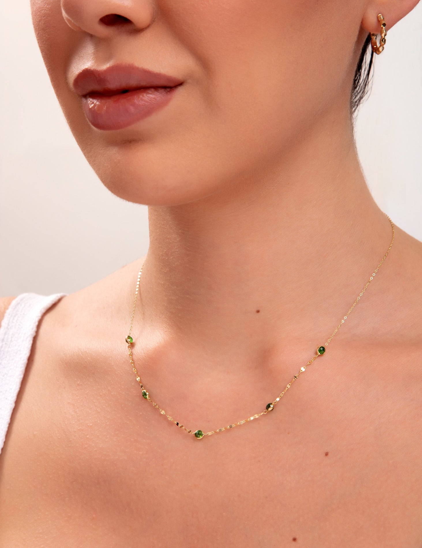 Model wearing gold necklace with green gemstones

